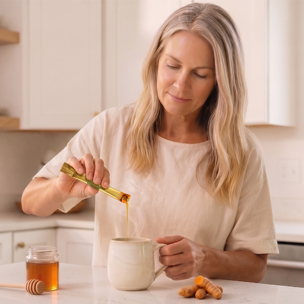 Woman pouring DailyRoot turmeric curcumin sachet into a mug, with honey and fresh turmeric root on the counter